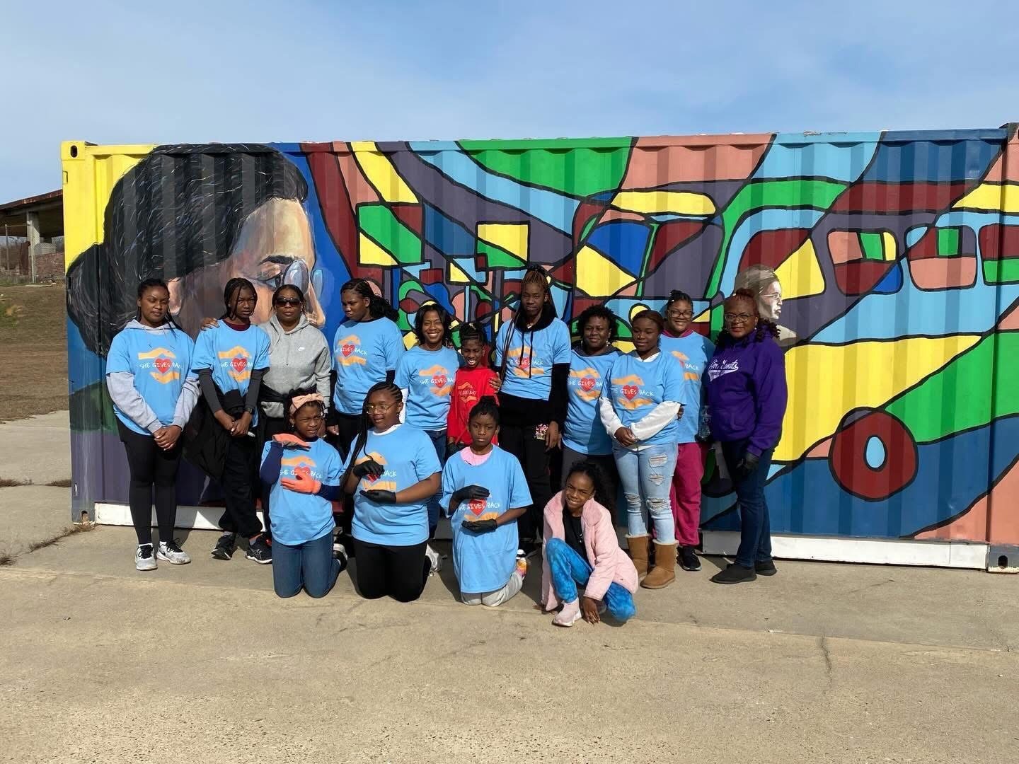 Girls in matching shirts in front of a colorful mural